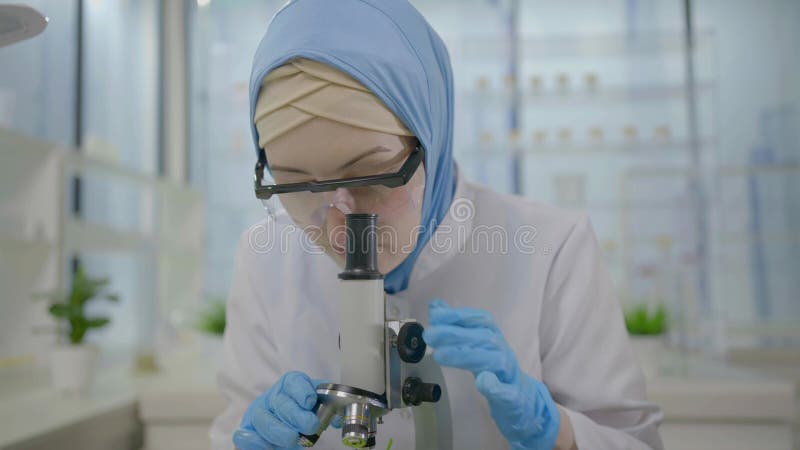 Musulmán científico del pañuelo en la cabeza en un laboratorio moderno trabaja en una laptop y un microscopio