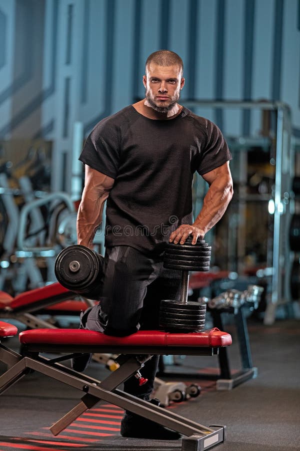 Musulär manlig idrottare som utför styrkeutbildning på ett modernt gym under kvällstid royaltyfri bild