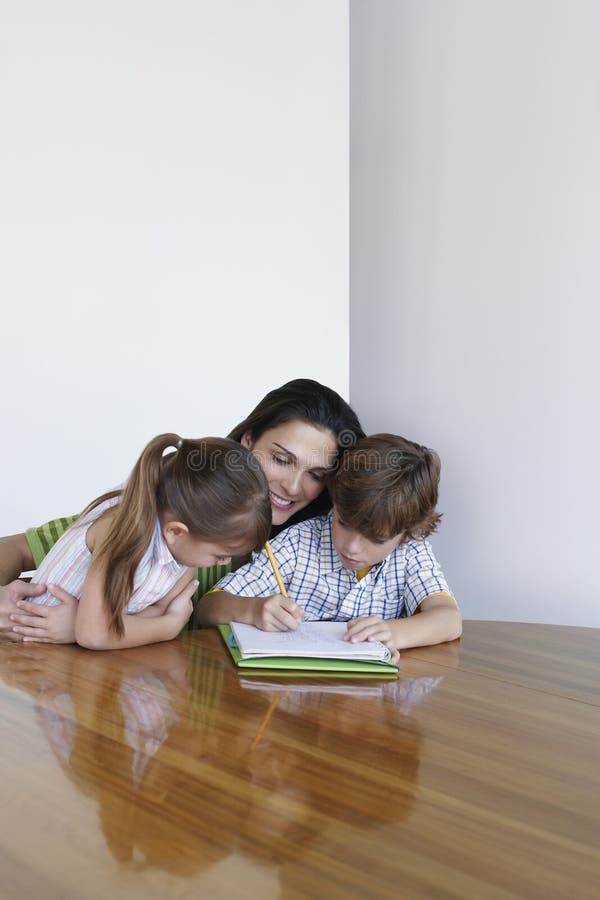 Mutter, die bei Tisch Kinder in der Hausarbeit unterstützt stockbild Mutter, die bei Tisch Kinder in der Hausarbeit unterstützt stockbild