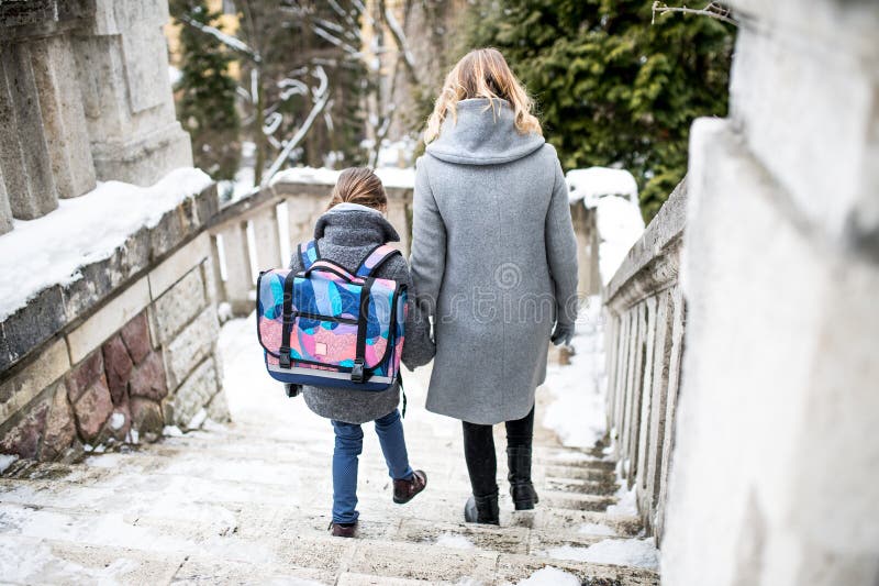 Mutter, die ihre Tochter aus der Grundschule abholt. nach einem langen Arbeitstag und in der Schule nach Hause gehen. Heckansicht. stockfotografie
