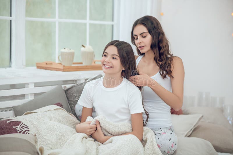 Mutter, die lange Haare lächelnder Tochter flicht lizenzfreie stockbilder