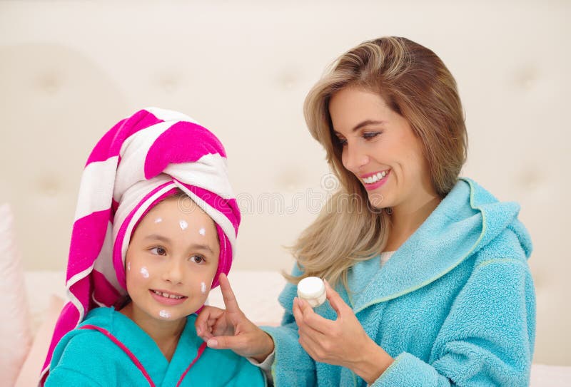 Mutter, die zu ihrer kleinen Tochter eine Creme im Gesicht, Tragen blaue Bademäntel im Raum aplying ist lizenzfreie stockfotografie