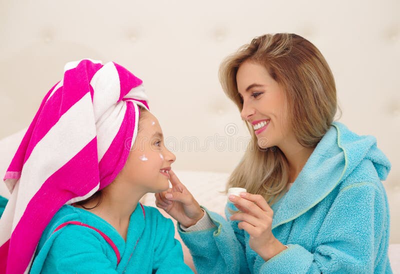 Mutter, die zu ihrer kleinen Tochter eine Creme im Gesicht, Tragen blaue Bademäntel im Raum aplying ist lizenzfreies stockfoto