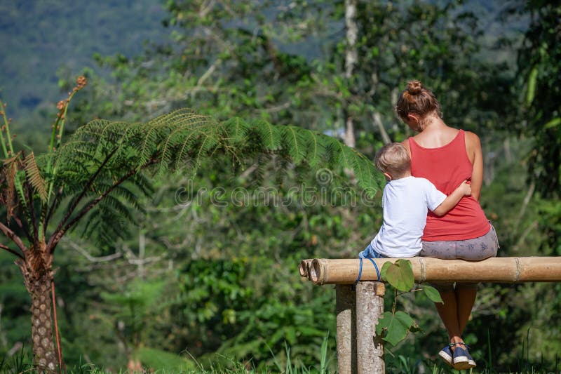 Mutter kleiner Sohn hat Spaß draußen auf der Bank unter dem Baum auf sonniger Rasen. stockbild