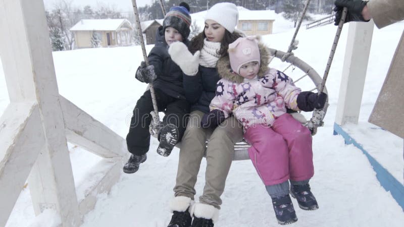 Mutter mit zwei Kindern auf großem Schwingen im Winter, slowmotion