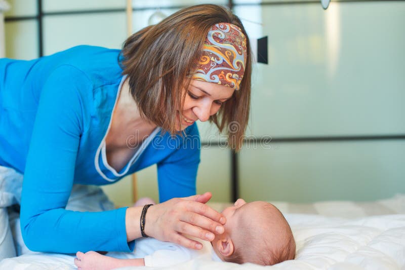 Mutter und Kind auf einem weißen Bett Mutter und Baby in der Windel, die im sonnigen Schlafzimmer spielt Mutter macht Gymnastik f stockfoto Mutter und Kind auf einem weißen Bett Mutter und Baby in der Windel, die im sonnigen Schlafzimmer spielt Mutter macht Gymnastik f stockfoto