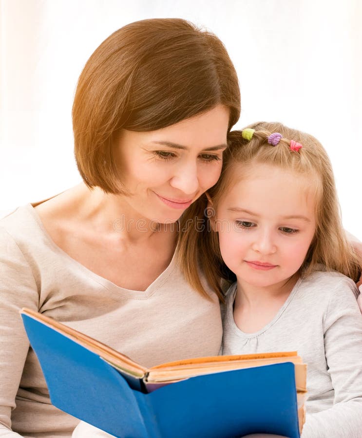 Mutter und kleines Tochterlesebuch, die auf Sofa im hellen Wohnzimmer sitzen Glückliche Familienzeit zusammen