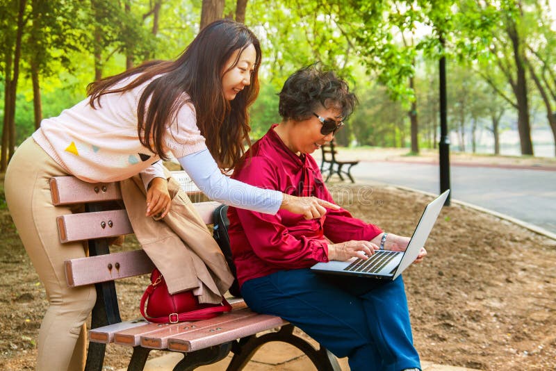 Mutter und Tochter, die einen Laptop am Garten verwendet Tochter unterrichtet eine ältere Mutter, einen Computer zu benutzen stockbild Mutter und Tochter, die einen Laptop am Garten verwendet Tochter unterrichtet eine ältere Mutter, einen Computer zu benutzen stockbild