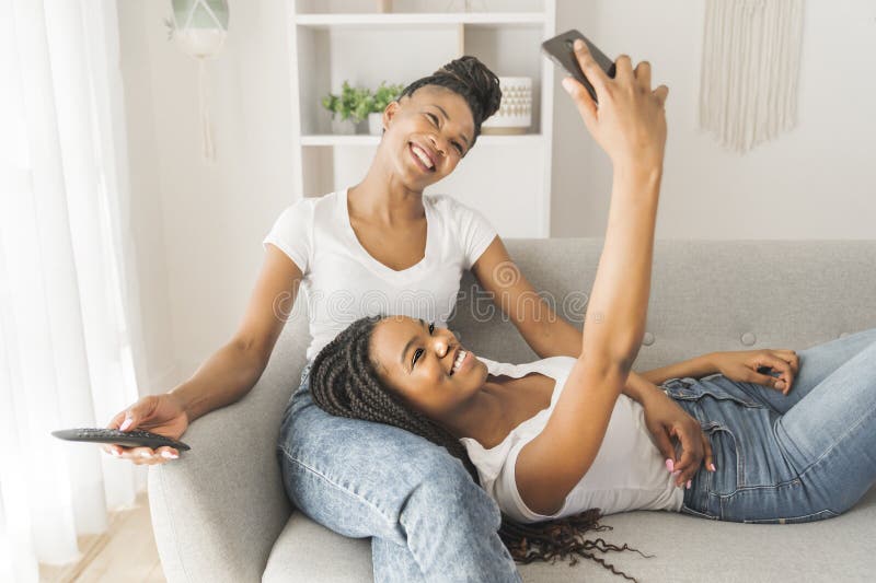 Mutter und Tochter, die zu Hause auf einem Sofa sitzen und sich selber ins Handy nehmen stockfotos