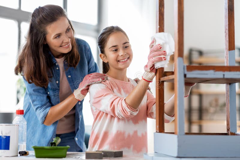 renovation, diy and home improvement concept - happy smiling mother and daughter cleaning old round wooden table surface with tissue. renovation, diy and home improvement concept - happy smiling mother and daughter cleaning old round wooden table surface with tissue