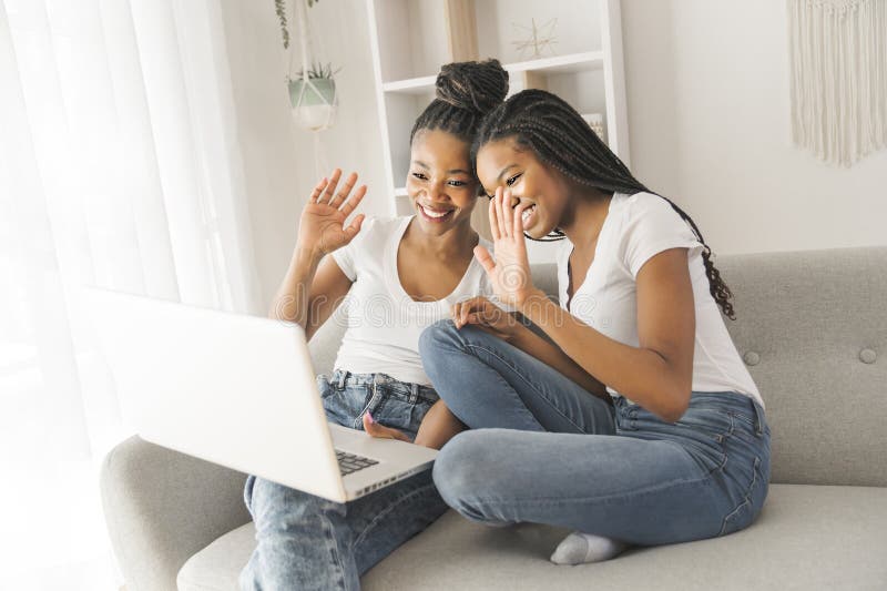 Mutter und Tochter sitzen zu Hause auf einem Sofa und sprechen mit einem Laptop mit einem Familienmitglied und sagen ihm stockfotografie
