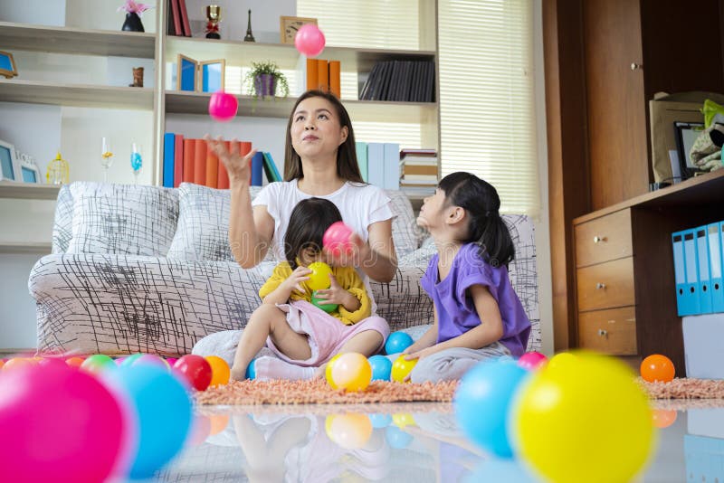 Mutter- und Tochterlächeln sind sie mit Windball. Mutter hat drei Bälle in der Luft. Die asiatischen Töchter einer Mutter zwei, die gerne zu Hause Mutter- und Tochterlächeln sind sie spielen, mit Windball.