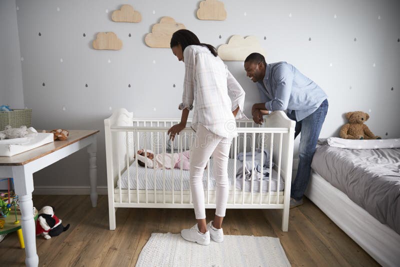 Mutter-und Vater-Looking At Baby-Tochter im Kindertagesstätten-Feldbett lizenzfreie stockbilder Mutter-und Vater-Looking At Baby-Tochter im Kindertagesstätten-Feldbett lizenzfreie stockbilder
