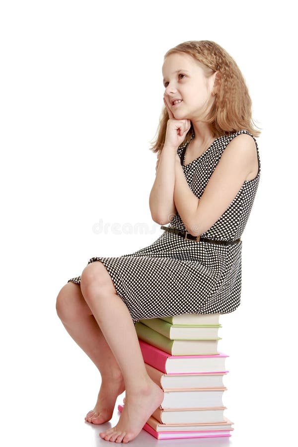 Very sweet, charming, light-haired teenage girl in a light gray silk dress sitting on a stack of books-Isolated on white background. Very sweet, charming, light-haired teenage girl in a light gray silk dress sitting on a stack of books-Isolated on white background