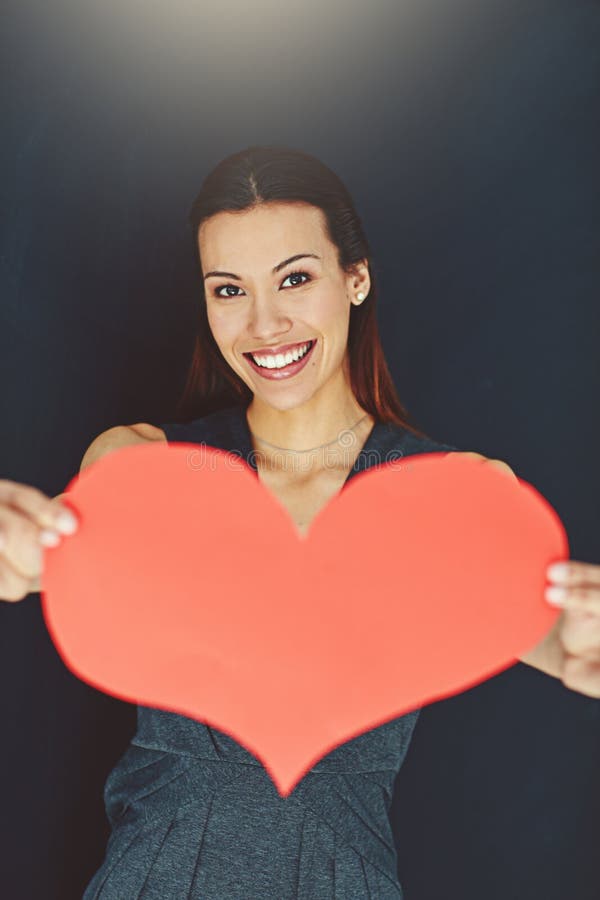 My heart is yours. Portrait of a young woman posing with a heart against a gray background. stock photography