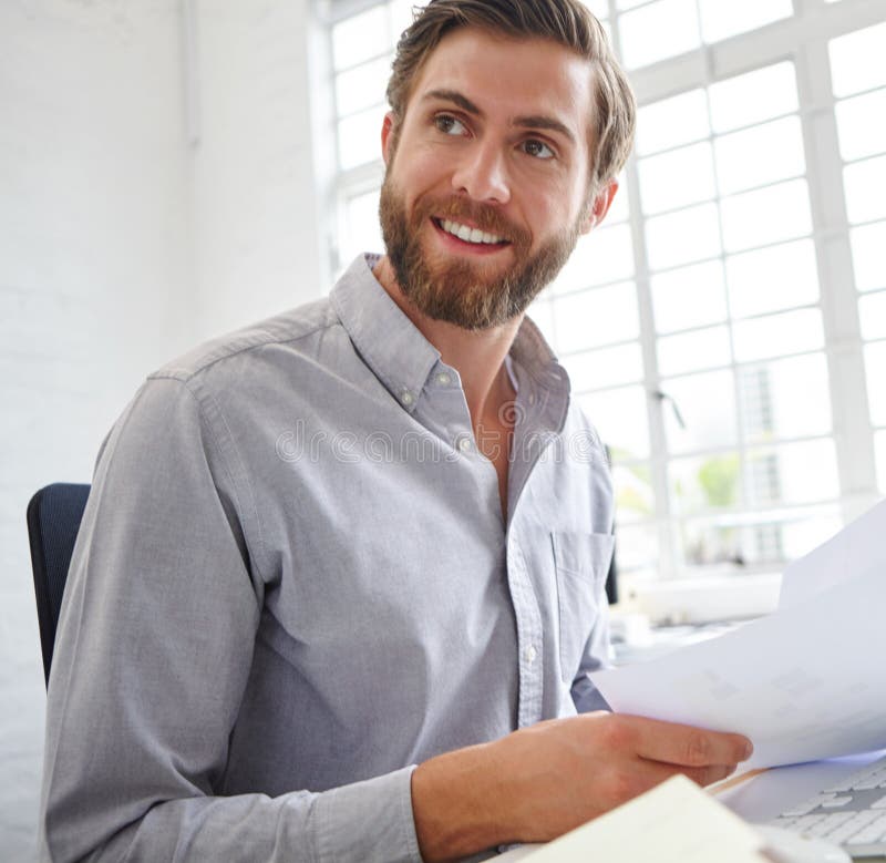 My team did a good job this month. a young designer holding paperwork while sitting in front of his computer. royalty free stock photo