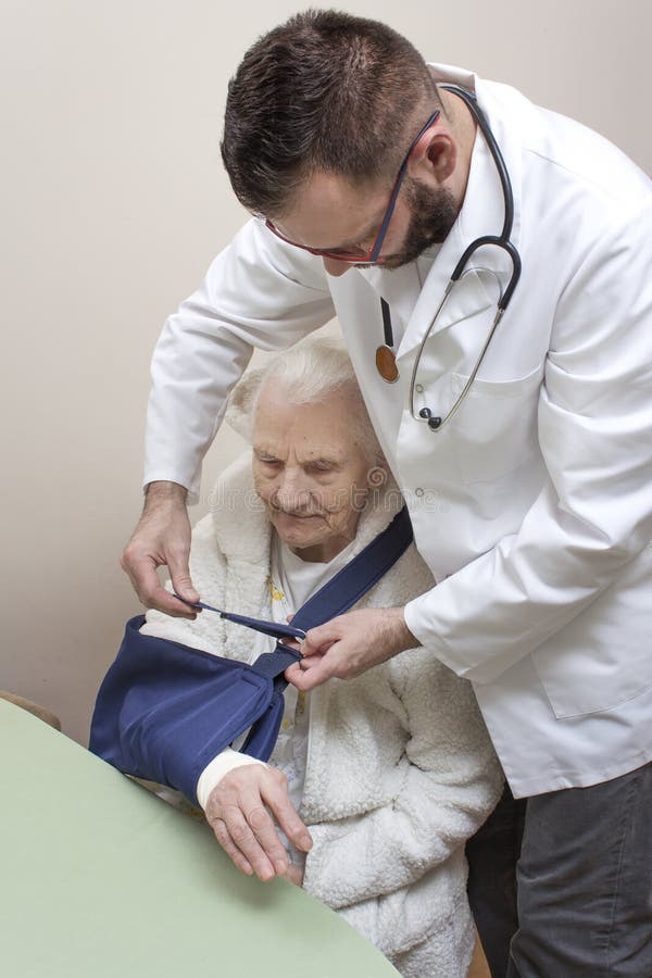 Mycket gammal gråhårig kvinna som sitter på en stol Doktorn sätter en rem på armen av en gammal kvinna arkivfoton Mycket gammal gråhårig kvinna som sitter på en stol Doktorn sätter en rem på armen av en gammal kvinna arkivfoton