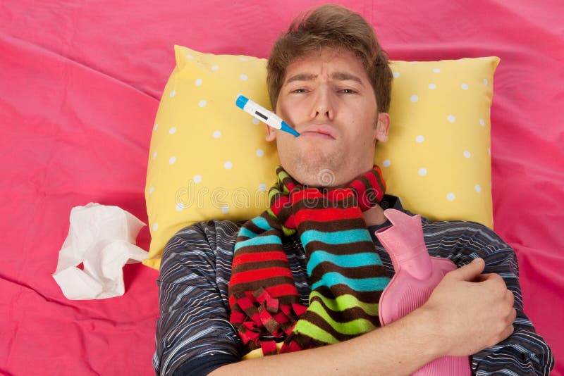 Very ill man is sitting in his bed with warm water bottle and thermometer. Very ill man is sitting in his bed with warm water bottle and thermometer