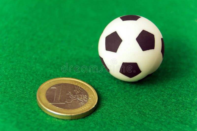 Concept money and sports, betting on football, corruption and earnings. Coin one euro and a souvenir soccer ball on a green background. Macro. Super close-up. Concept money and sports, betting on football, corruption and earnings. Coin one euro and a souvenir soccer ball on a green background. Macro. Super close-up.