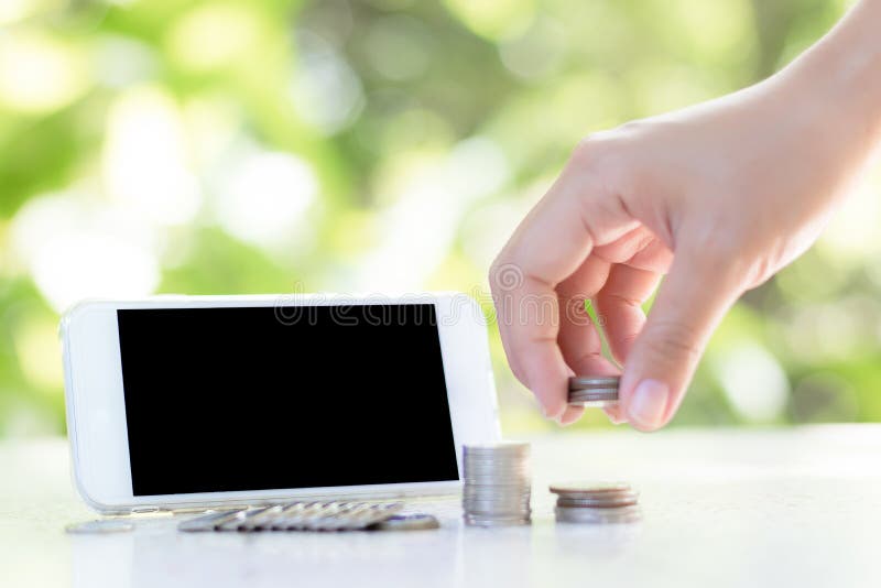 The hands are putting the coins in rows And there is a telephone placed behind Green natural background Represents business, finance and technology. The hands are putting the coins in rows And there is a telephone placed behind Green natural background Represents business, finance and technology.