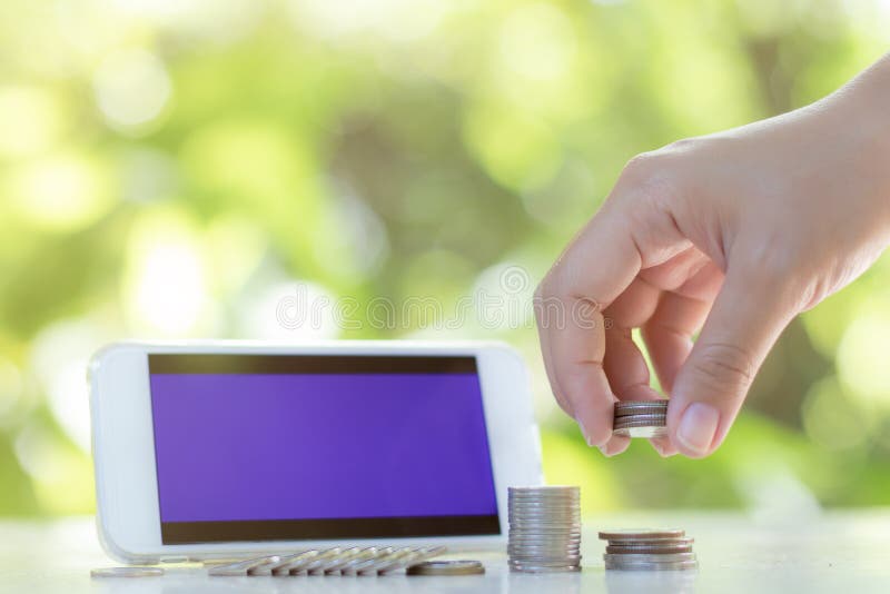 The hands are putting the coins in rows And there is a telephone placed behind Green natural background Represents business, finance and technology. The hands are putting the coins in rows And there is a telephone placed behind Green natural background Represents business, finance and technology.