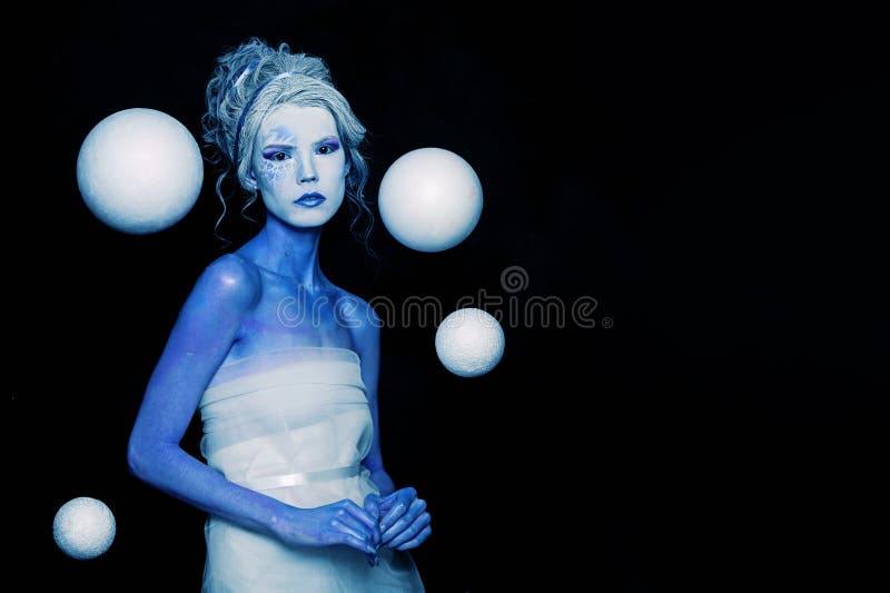 Mysterious cool cold woman with blue and white body art, carnival makeup and white space planet sphere on black background