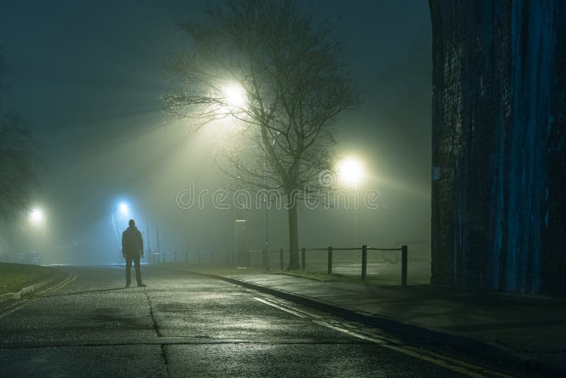 A mysterious figure standing by a city street light on a moody,  foggy atmospheric winters night