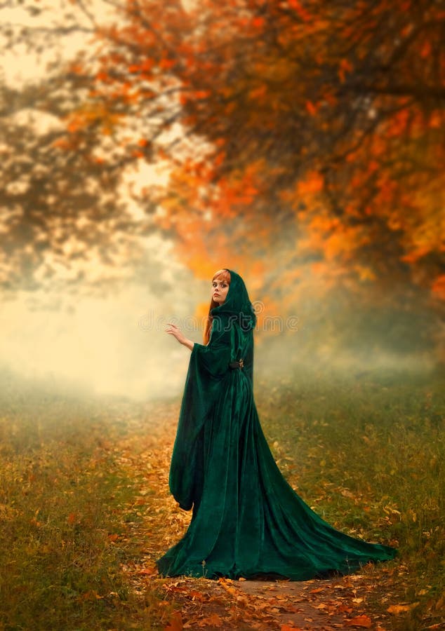 Mysterious stranger the girl turned around on a path in the forest, in a green emerald dress with a hood and wide