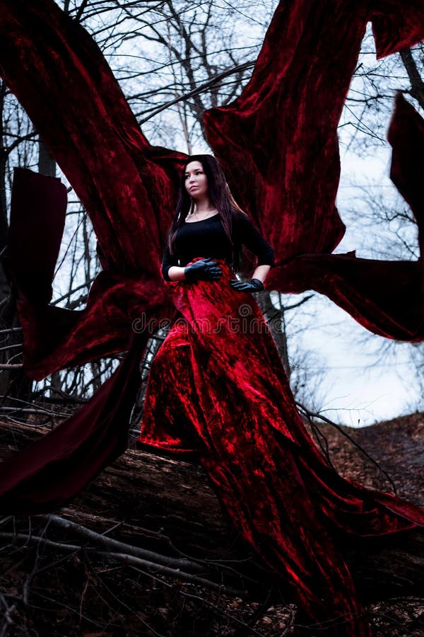 Mysterious Woman Or Witch In Long Red Dress Standing In Dark Forest