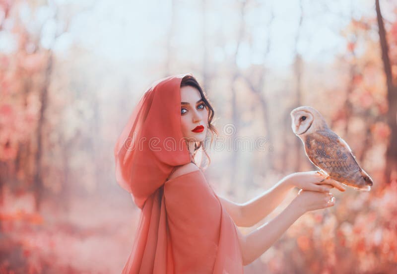 Mystical pagan woman with covered head in peach scarf in forest, holds barn ow