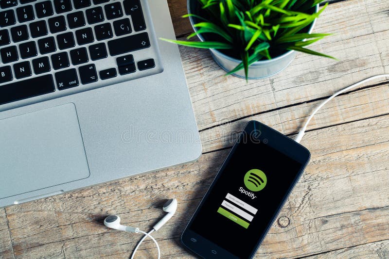 MÁLAGA, ESPAÑA - 29 DE OCTUBRE DE 2015: Spotify app en un teléfono móvil, cerca de un ordenador, en un escritorio de madera foto de archivo libre de regalías