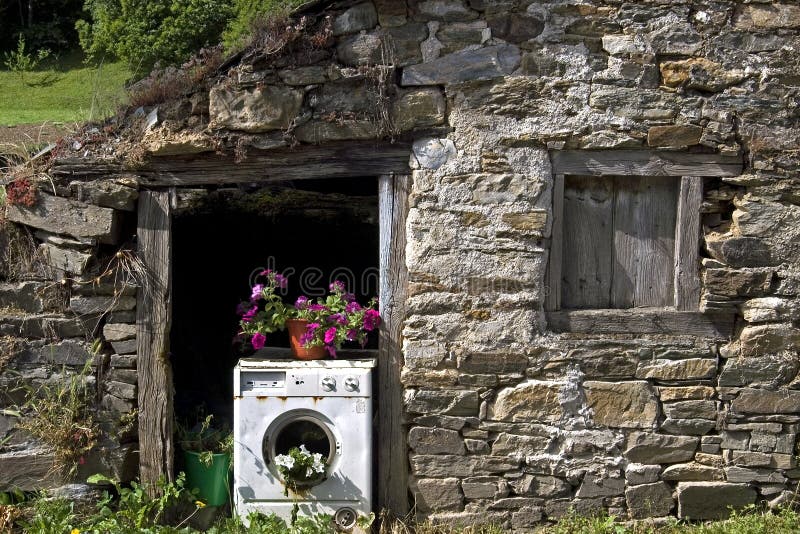 Spain, county, province of Leon, autonomous, community Castile and Leon. Town, village, Hospital Ingles. Still life of an old barn, built of stone boulders. In the doorway is a broken fully automatic washing machine, which is recycled into a flowerpot, planter. At least there are several flower pots inside with vibrant, growing, and flowers on top. Spain, county, province of Leon, autonomous, community Castile and Leon. Town, village, Hospital Ingles. Still life of an old barn, built of stone boulders. In the doorway is a broken fully automatic washing machine, which is recycled into a flowerpot, planter. At least there are several flower pots inside with vibrant, growing, and flowers on top.