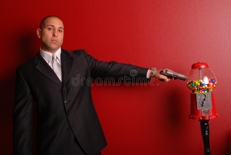 Attractive man wearing a business suit pointing a gun at a gumball machine. Attractive man wearing a business suit pointing a gun at a gumball machine.