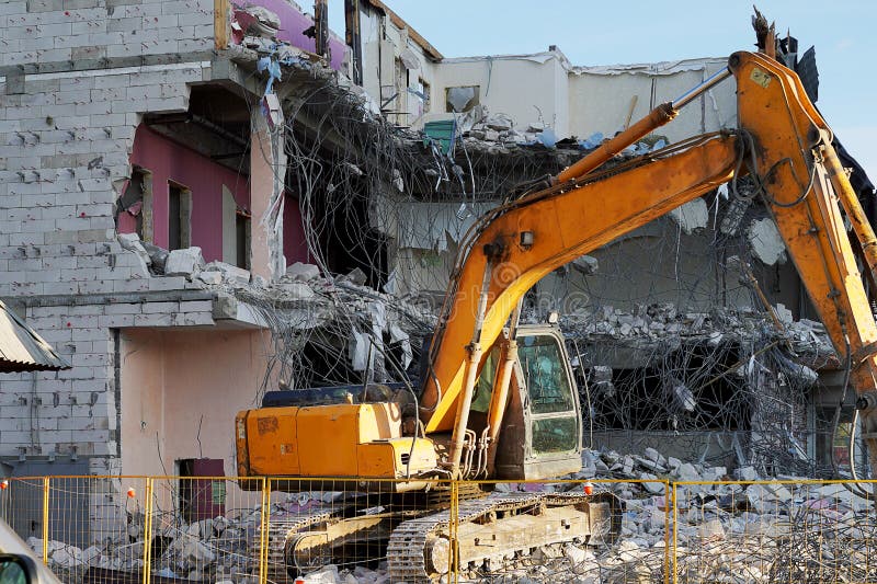 Máquina escavadora amarela que demole uma construção do multi-andar Os assoalhos destruídos da construção, são partes de pedra, c imagens de stock