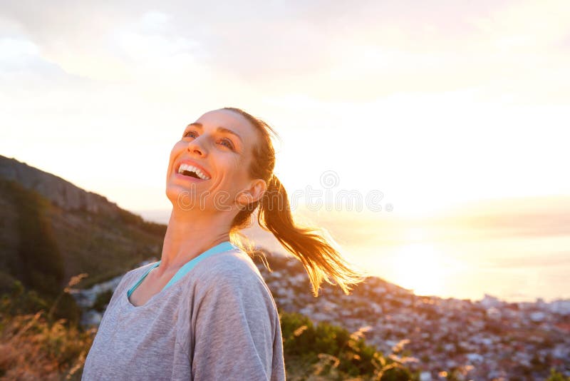 Más vieja mujer atractiva que ríe al aire libre durante puesta del sol