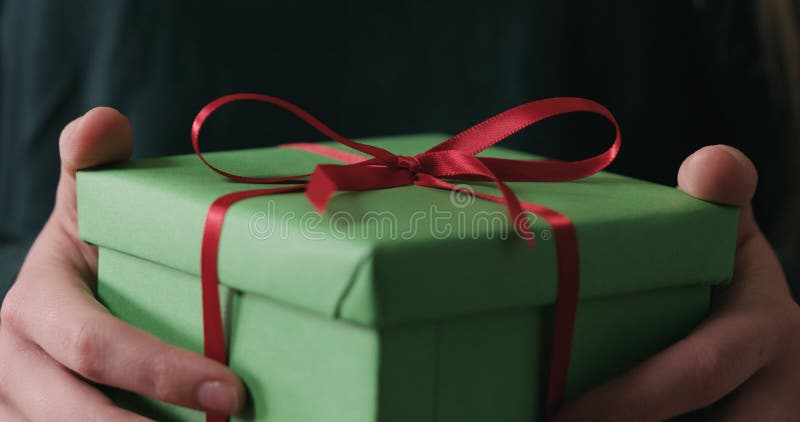 Mâinile femele apropiate arată un cadou verde cu fundă roșie stock photo