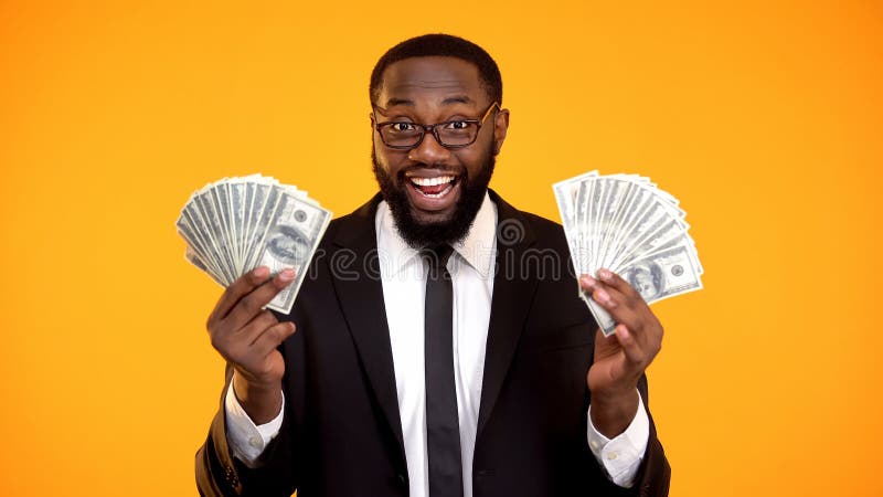 Mâle afro-américain heureux dans le costume montrant des groupes d'argent liquide du dollar, bénéfice images stock