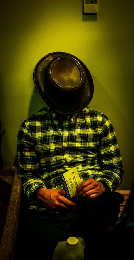Mâle dans une chemise de flanelle et un chapeau de cowboy dormant tout en se reposant près d'un mur photos stock Mâle dans une chemise de flanelle et un chapeau de cowboy dormant tout en se reposant près d'un mur photos stock