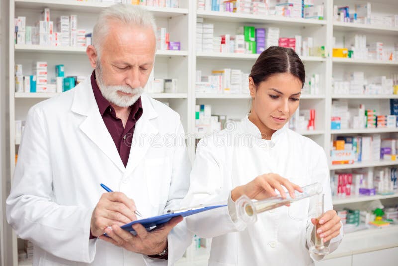 Mâle supérieur et jeunes pharmaciens féminins mélangeant des produits chimiques dans une pharmacie image libre de droits Mâle supérieur et jeunes pharmaciens féminins mélangeant des produits chimiques dans une pharmacie image libre de droits