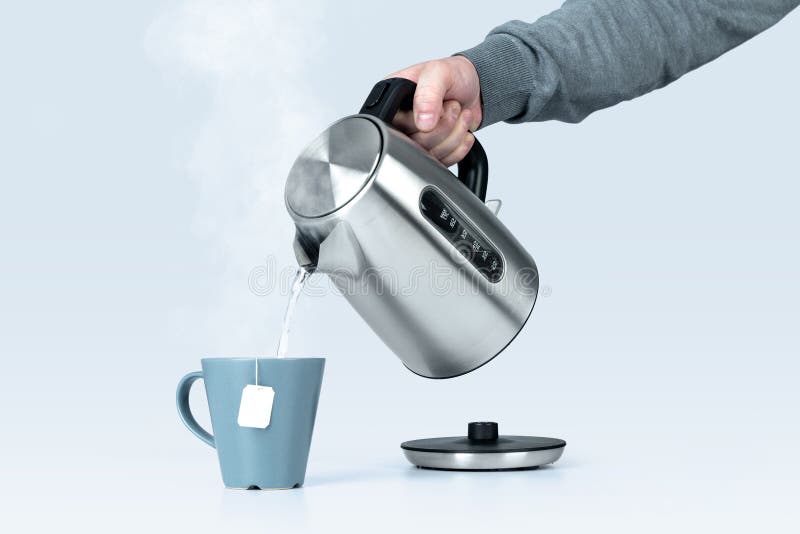 Mâna unui bărbat care ține un ceainic electric care toarnă apă caldă într-o cană cu un sac de ceai pe fond albastru deschis. royalty free stock image