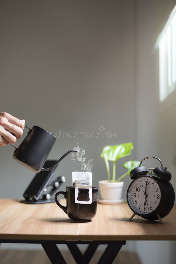 Mână care ține un ceainic turnând apă fierbinte într-o ceașcă de cafea dimineața lângă fereastră. stock image
