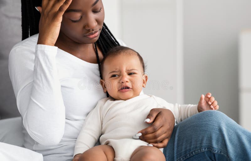 Mãe africana estressada sentada com uma criança na cama