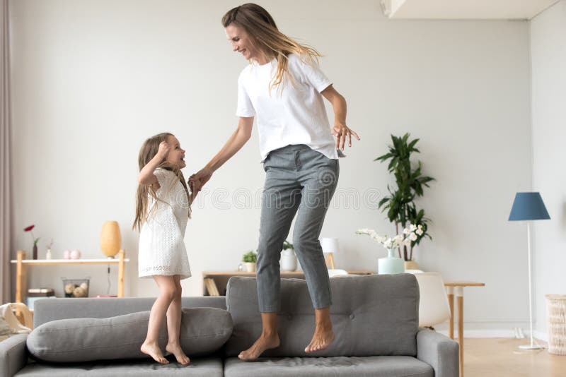 Mãe alegre e filha que saltam no sofá em casa fotos de stock Mãe alegre e filha que saltam no sofá em casa fotos de stock