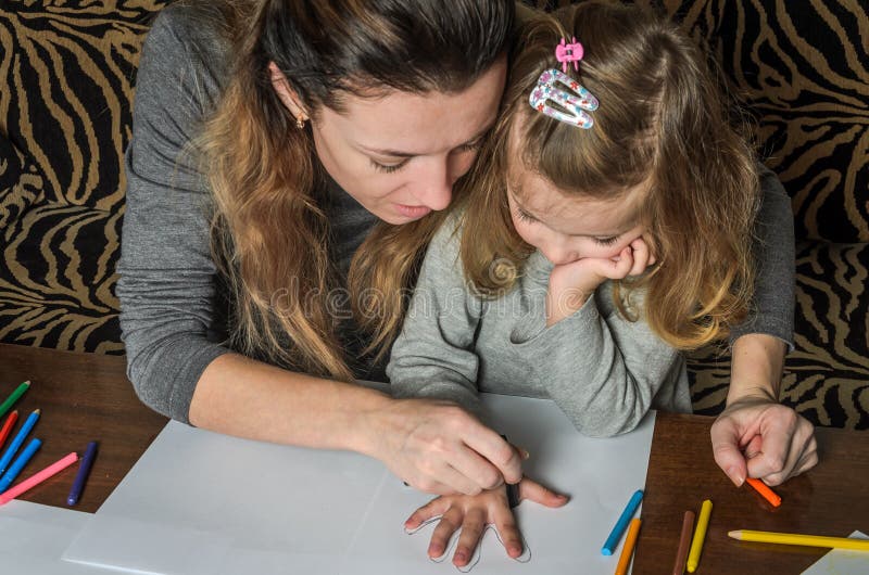 Mãe bonita nova com sua tração da filha com os lápis coloridos no papel, família feliz imagens de stock Mãe bonita nova com sua tração da filha com os lápis coloridos no papel, família feliz imagens de stock