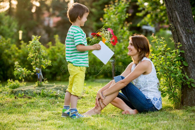 Mãe bonita nova, sentando-se em um jardim, rapaz pequeno, seu filho fotografia de stock royalty free Mãe bonita nova, sentando-se em um jardim, rapaz pequeno, seu filho fotografia de stock royalty free