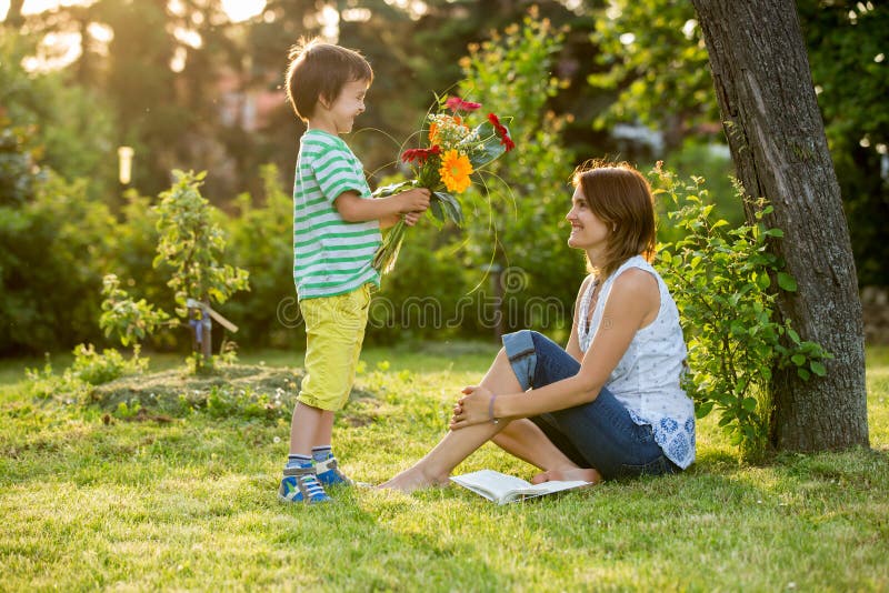 Mãe bonita nova, sentando-se em um jardim, rapaz pequeno, seu filho imagem de stock Mãe bonita nova, sentando-se em um jardim, rapaz pequeno, seu filho imagem de stock