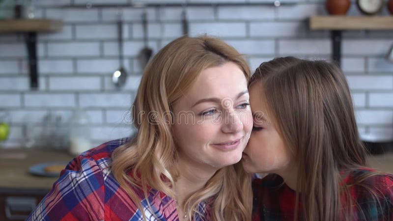 A mãe brincalhão e a filha têm o divertimento na cozinha junto A menina beija sua mãe e fricciona seu mordente