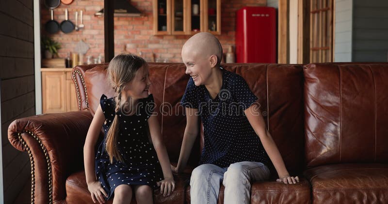 Mãe careca, sua filha brincando, pulando sentada no sofá