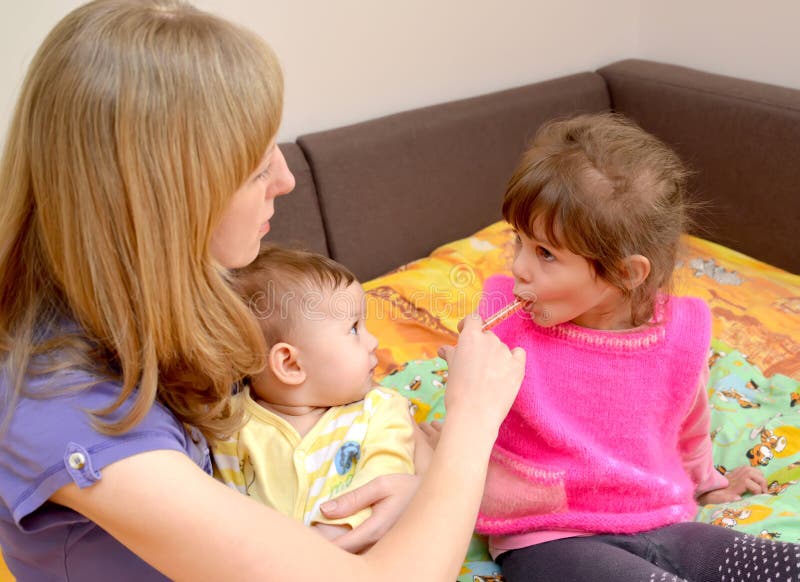 A mãe com o bebê nas mãos dá à medicina doente da menina por meio do batcher tratamento imagens de stock A mãe com o bebê nas mãos dá à medicina doente da menina por meio do batcher tratamento imagens de stock