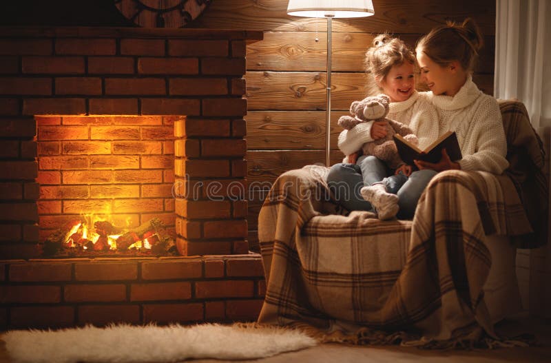 A mãe da família e a filha felizes da criança leram o livro no eveni do inverno